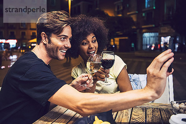 Mann  der ein Selfie mit seiner Freundin macht  während er mit ihr bei einem Date auf den Wein anstößt
