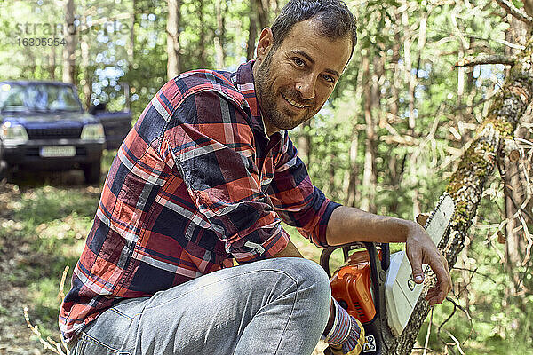 Lächelnder Holzfäller mit Kettensäge auf einem Ast im Wald