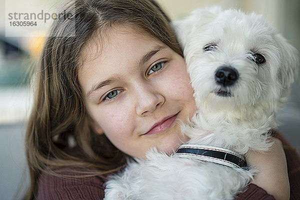 Nettes lächelndes Mädchen umarmt Hund im Wohnzimmer