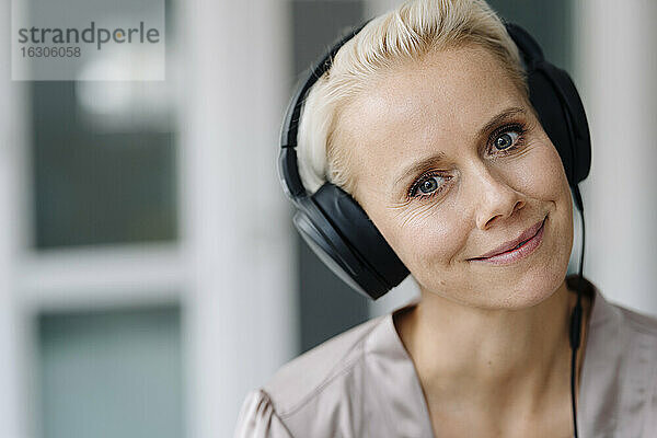 Nahaufnahme einer lächelnden Geschäftsfrau  die im Büro über Kopfhörer Musik hört
