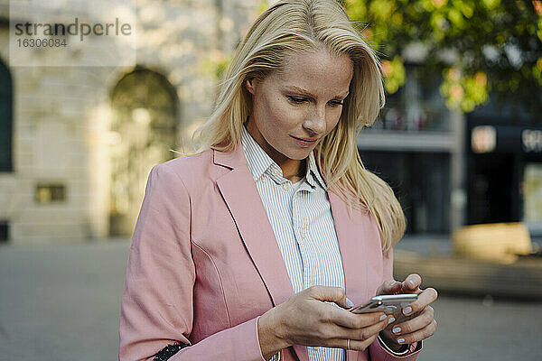 Schöne blonde Frau  die ein Smartphone im Finanzviertel der Stadt benutzt