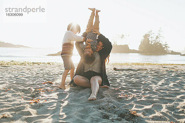 Mutter spielt mit Kindern  während sie im Sand am Strand sitzt