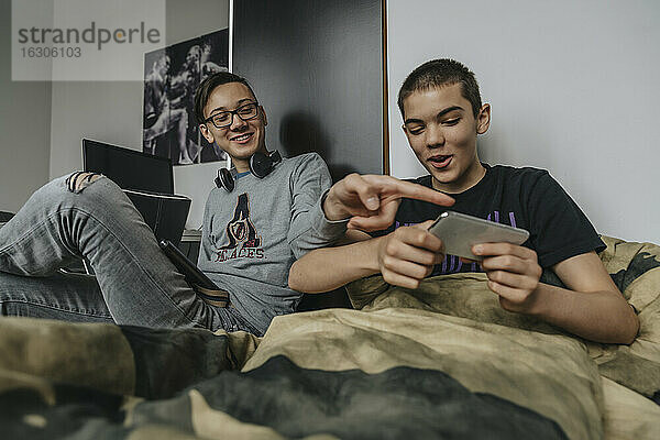 Teenager auf dem Bett sitzend  die sich mit tragbaren Geräten vergnügen