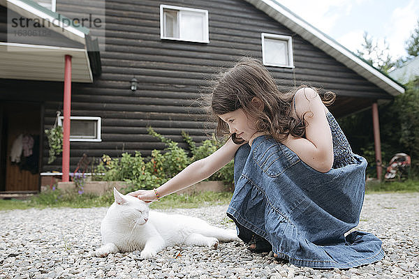 Kleines Mädchen streichelt Katze im Vorgarten des Hauses