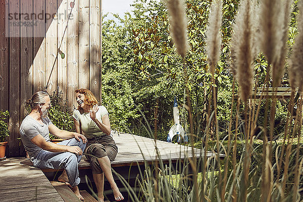 Fröhliches Paar unterhält sich  während es vor einem kleinen Haus im Hof sitzt