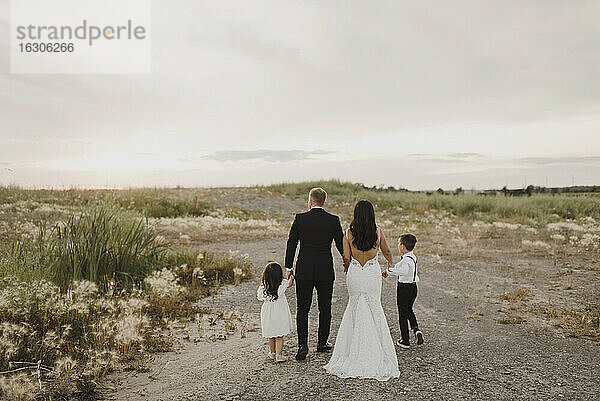 Eltern und Kinder im Hochzeitskleid beim Spaziergang im Feld gegen den Himmel