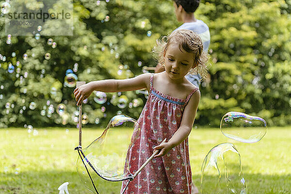 Süßes Baby Mädchen macht Blase mit Bruder im Hintergrund im Park