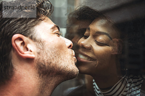 Nahaufnahme eines romantischen Mannes  der seine Freundin durch ein Glasfenster küsst