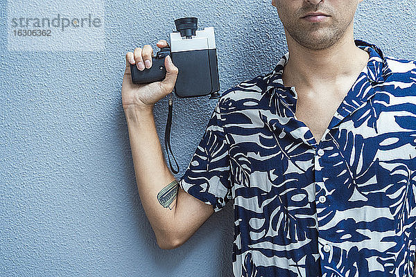 Mann hält Filmkamera gegen blaue Wand