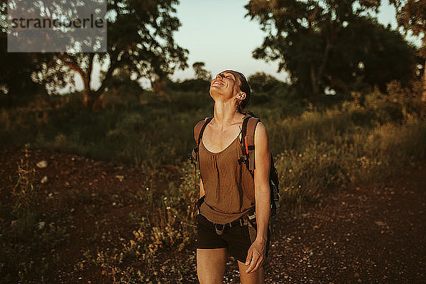 Lächelnde Frau mit zurückgelegtem Kopf beim Wandern im Wald