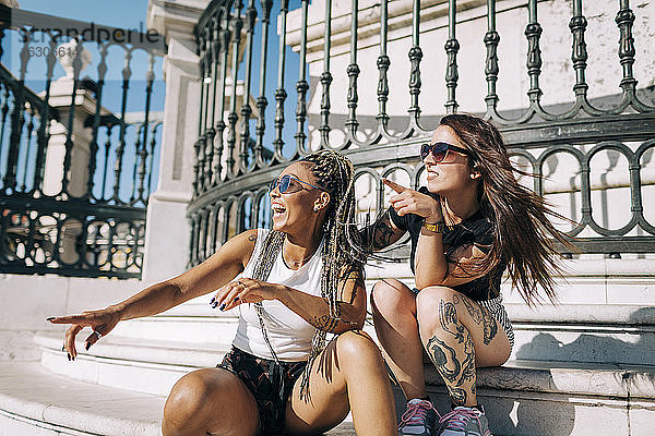 Freundinnen lachen  während sie gegen einen Zaun am Praca Do Comercio zeigen  Lissabon  Portugal