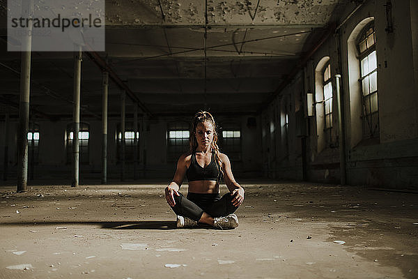 Sportler meditiert sitzend in einer verlassenen Fabrik