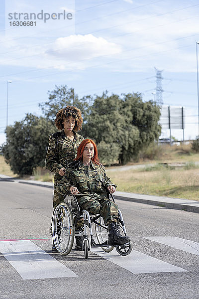 Ein Soldat hilft einem behinderten Militärangehörigen im Rollstuhl  während er auf der Straße steht