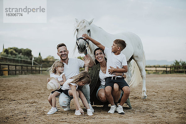 Fröhliche Eltern mit Kindern  die bei einem Pferd in der Scheune hocken