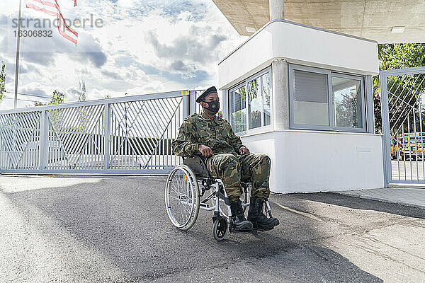 Armeesoldat mit Gesichtsschutzmaske im Rollstuhl sitzend vor bewölktem Himmel