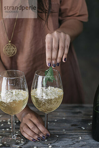 Mittelteil einer Frau  die bei der Zubereitung eines Cocktails Minzblätter über ein Weinglas hält