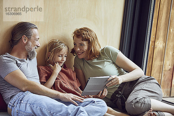 Lächelnde Eltern mit Tochter  die ein digitales Tablet benutzt  während sie sich zu Hause auf dem Bett entspannen
