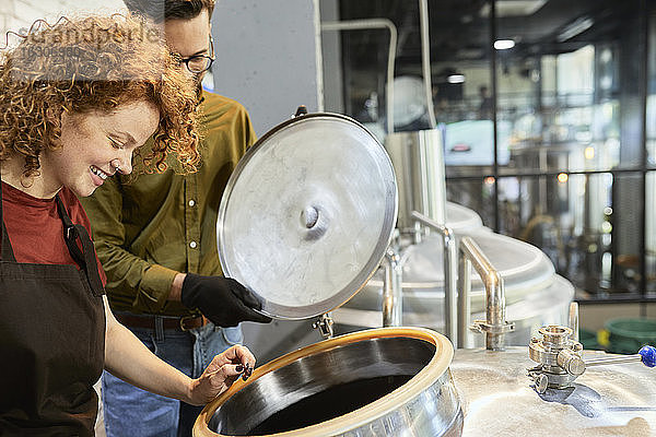 Mann und Frau arbeiten in einer Handwerksbrauerei und schauen in den Tank