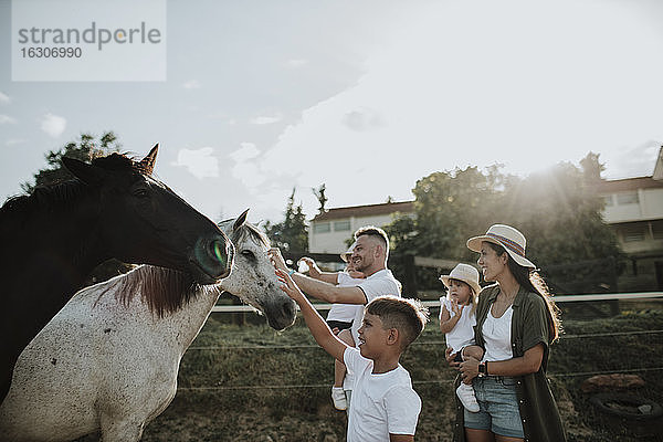 Familie berührt Pferde und steht gegen den Himmel