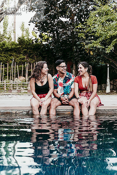 Lächelnde Freunde  die am Pool sitzen und sich unterhalten