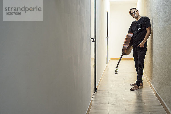Selbstbewusster Musiker  der eine Gitarre hält  während er im Korridor steht