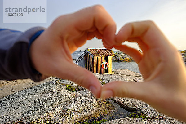 Schweden  Bezirk Vastra Gotaland  Grebbestad  Hände eines Mädchens  das ein Herz gegen eine Hütte am felsigen Ufer des Tjurpannans Naturreservats formt