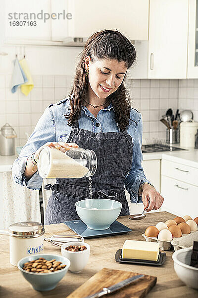 Schöne Frau wiegt Mehl auf Küchenwaage für Backen Kuchen zu Hause