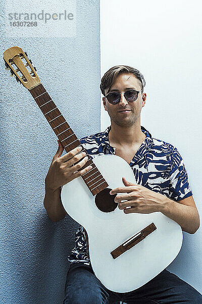 Lächelnder Musiker hält Gitarre gegen blaue Wand