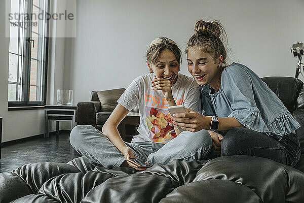 Fröhliche Freunde benutzen ein Smartphone  während sie sich zu Hause auf der Couch entspannen