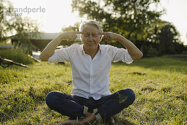 Mann mit geschlossenen Augen  der im Hinterhof sitzend Yoga praktiziert