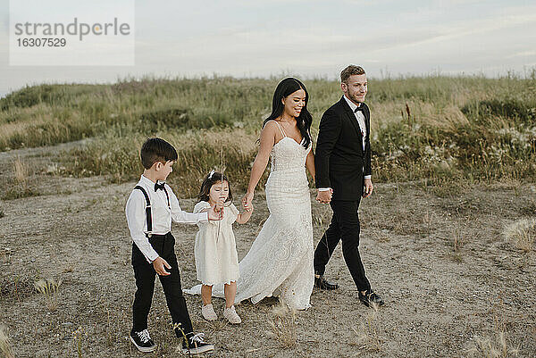 Eltern mit Kindern im Hochzeitskleid beim Spaziergang im Feld