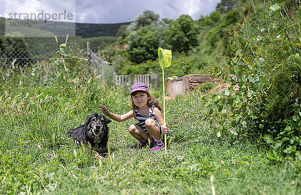 Nettes Mädchen hockt bei Hund in grünem Feld während sonnigen Tag