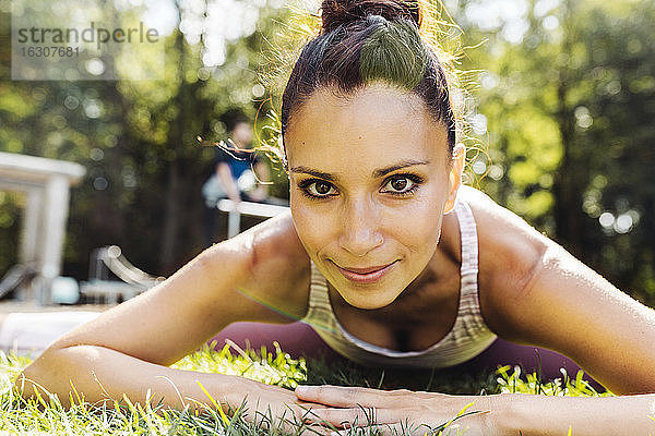 Porträt einer Frau  die sich im Gras in der Nähe eines Fitnessparcours dehnt