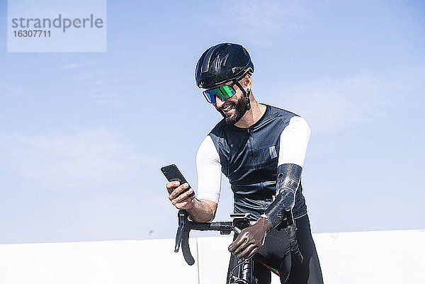 Männlicher amputierter Sportler  der ein Mobiltelefon benutzt  während er mit dem Fahrrad vor einem klaren Himmel steht