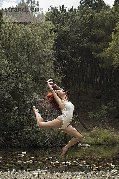 Mittlere erwachsene Frau übt Akrobatik am Seeufer im Wald
