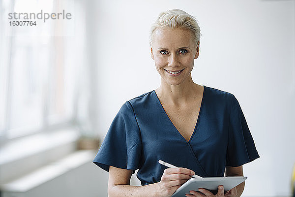 Lächelnde Geschäftsfrau  die im Büro stehend über einem digitalen Tablet arbeitet