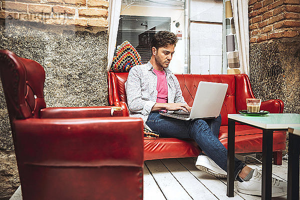 Mittlerer erwachsener Mann  der einen Laptop benutzt  während er auf dem Sofa in einem Café sitzt