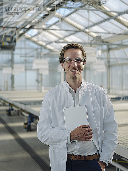 Porträt eines lächelnden Wissenschaftlers mit Tablette in einem Gewächshaus