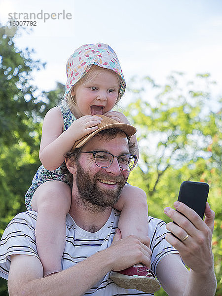 Tochter streckt die Zunge heraus  während der Vater ein Selfie mit dem Smartphone macht
