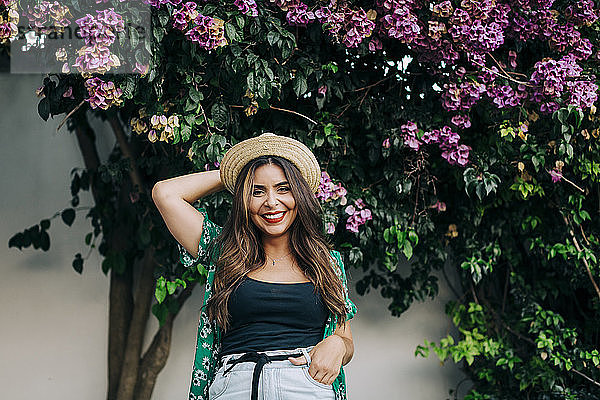 Fröhliche junge Frau mit Hut vor Pflanzen stehend
