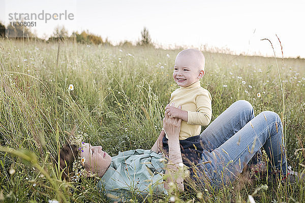 Glücklicher Junge  der auf seiner Mutter sitzt  die auf einer Wiese liegt  während eines sonnigen Tages