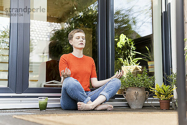 Mittlere erwachsene Frau meditiert  während sie auf einer Veranda gegen das Haus sitzt