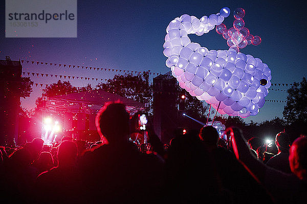 Wal aus lilafarbenen Luftballons schwebt über einer Menschenmenge  die sich bei einem nächtlichen Musikfestival amüsiert