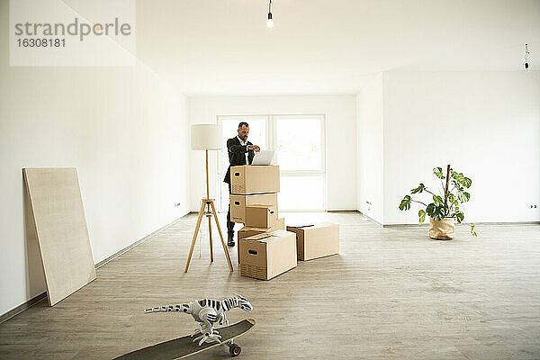 Geschäftsmann  der einen Laptop auf einer Box benutzt  während er in einer neuen  unmöblierten Wohnung steht