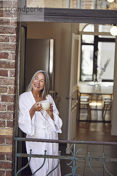 Glückliche Frau trinkt Tee auf dem Balkon