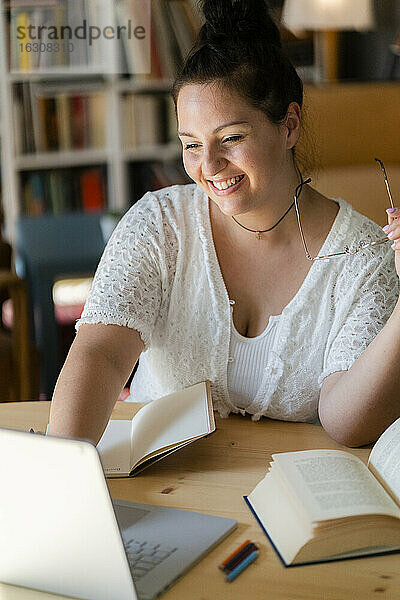 Lächelnde junge Frau studiert über einem Laptop auf einem Tisch in einem Café