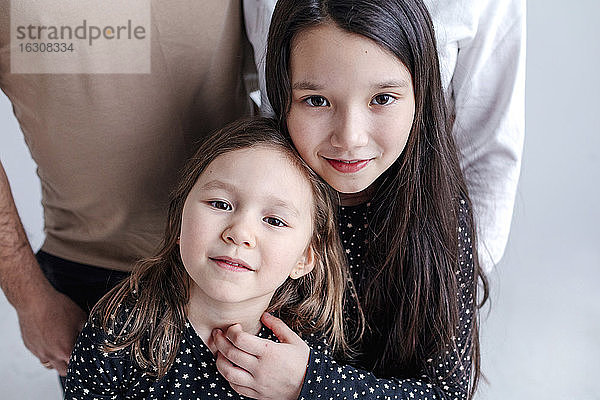 Mädchen umarmt Schwester mit Eltern stehen im Hintergrund im Studio