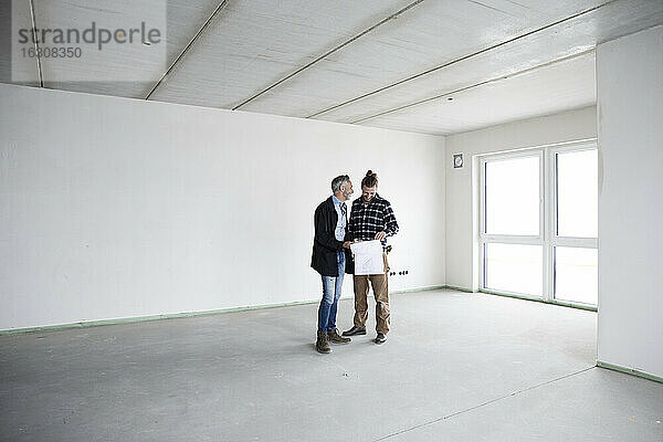 Architekt und Bauarbeiter besprechen einen Bauplan  während sie in einem leeren Haus stehen