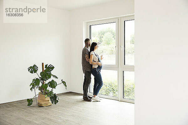 Paar  das durch ein Fenster schaut und neben einer Zimmerpflanze in einem neuen Haus steht