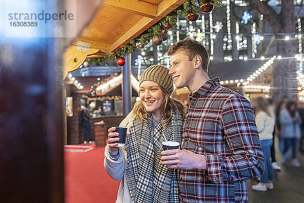 Ehepaar genießt heiße Schokolade auf dem nächtlichen Weihnachtsmarkt